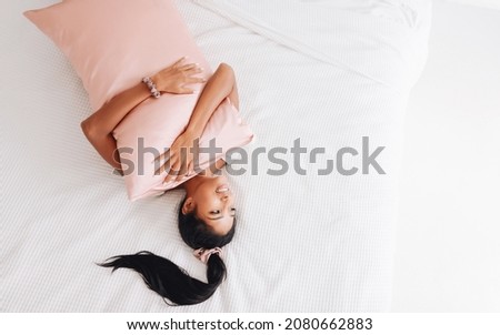 Beautiful Indonesian girl lying on a pink pillow with a silk pillowcase. View from above
 Royalty-Free Stock Photo #2080662883