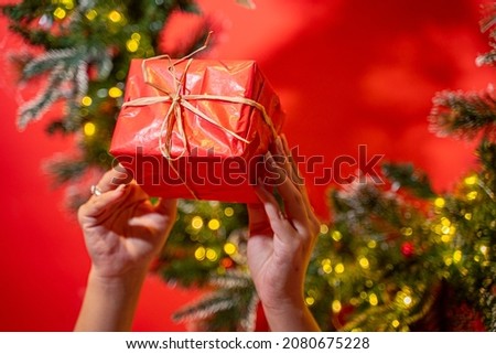 Two hands holding a present wrapped in red paper, with Christmas decorations in the background