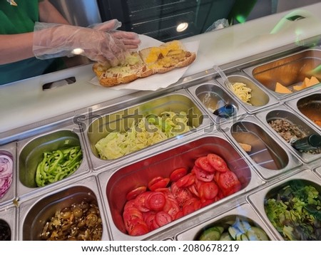 Fresh sandwich bar counter with person's hands cooks salad at sandwiches restaurant. for healthy and diet meal with smooth light and shadow. Royalty-Free Stock Photo #2080678219