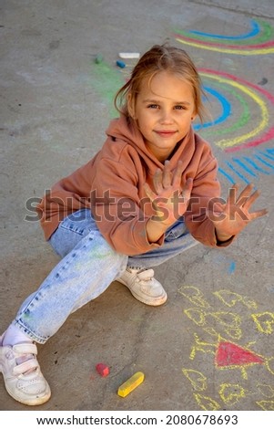 selective focus on the chalk-stained hands of a child girl blonde 7 years old after drawing pictures on the asphalt against the background of hearts and rainbow creativity of children on the street