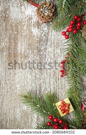 Christmas tree branches, gift box, conifer cones and red berries top view with copy space on old wooden background. Christmas, winter holiday, new year concept.