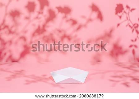 Abstract minimal nature scene - empty stage and polygonal podium on pastel pink background and soft rose flowers shadows. Pedestal for cosmetic product and packaging mockups display presentation