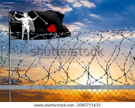 A fence with barbed wire against the background of a colorful sky and a flagpole with the flag of Blackbeard Pirate protects the state's border from illegal migration.