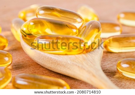 Cod liver oil omega 3 gel capsules on a spoon on wooden background. Fish oil vitamins.