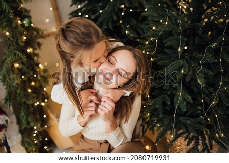 daughter kisses and hugs mother on a background of christmas trees with garland lights