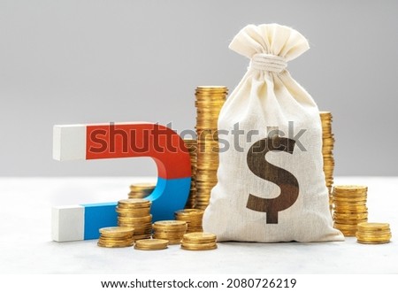 Magnet attracts money. Magnet and a stack of coins with money bag.