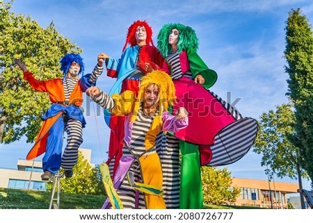 Low angle of cheerful male and female clowns in colorful costumes and wigs, smiling while performing show on stilts and unicycle during festival in city park Royalty-Free Stock Photo #2080726777