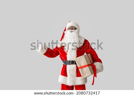African-American Santa Claus with gift on light background Royalty-Free Stock Photo #2080732417