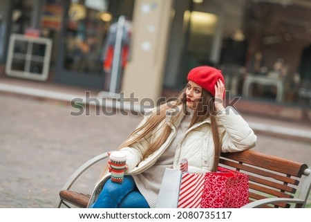 Street style portrait of young beautiful fashion woman walking in European city on winter holidays, holding Christmas bags. Stylish model in casual clothes with long hair.