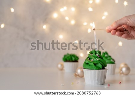 Merry christmas and happy new year. Green Christmas tree shaped cupcakes, surrounded with festive decorations and lights on the background