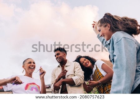 Four multicultural friends dancing on the rooftop. Group of happy young friends laughing and having a good time during a party. Vibrant young people having fun together on the weekend. Royalty-Free Stock Photo #2080757623