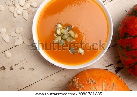 Food photography for halloween. Pumpkin seeds in a white plate with pumpkin soup. Pumpkins on a wooden vintage table with scuffs. Top view
