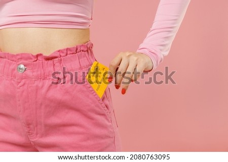 Cropped close up photo shot woman 20s in rosy top shirt hold in hand put credit bank card into pocket isolated on plain light pastel pink background studio portrait. People lifestyle fashion concept