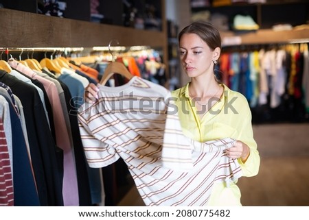 Pretty woman chooses fashionable t-shirt in store. High quality photo