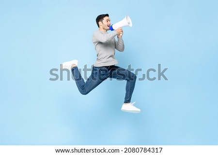 Portrait of energetic young Caucasian man jumping with megaphone isolated on light blue background Royalty-Free Stock Photo #2080784317