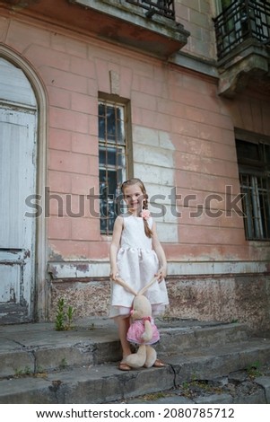 Beautiful young girl in white dress and pretty hairstyle holding a toy bunny