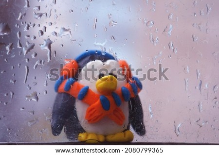 Penguin figurine on the background of a wet window.