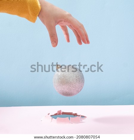 A womans hand grabs silver shiny bauble on pink and blue background. Minimal art. New year 2022 composition. Realistic aesthetic look.