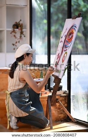 Portrait of female artist painting on canvas with color water in art studio.