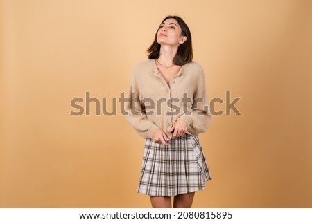 Young woman on a beige background in a soft cozy sweater with daytime professional make-up smiling cute, slim, good shape