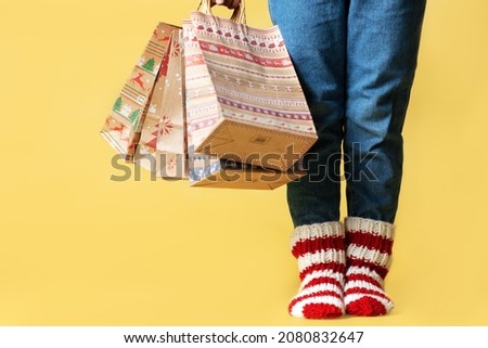 Delivery Christmas gifts shopping craft paper bags presents and child in knitted striped socks isolated yellow background