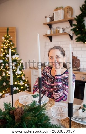 Mature woman in New Year's sweater setting  festive table. 