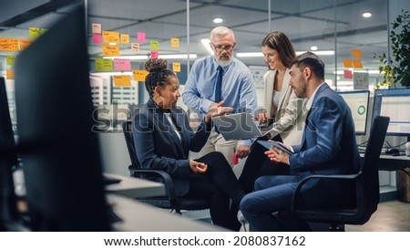 In Modern Office: Diverse Team of Managers Use Laptop and Tablet Computers at a Company Meeting Discussing Business Projects. Young, Motivated and Experienced Employees Brainstorm in Conference Room.