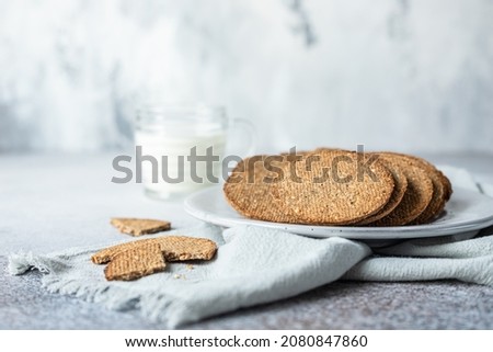 Plate with tasty crackers and a cup of milk. Snack or breakfast on grey stone background.