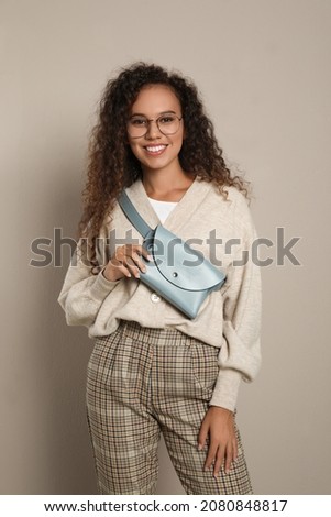 Beautiful African American woman with stylish waist bag on beige background