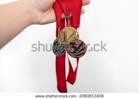Person is holding gold, silver and bronze medals  with numbers on white isolated background for winners.Medal with red ribbons.