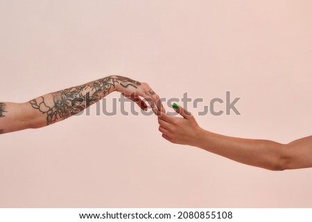 Closeup of two female arms reaching each other hand isolated over light pink background. Lgbtq, youth, love concept Royalty-Free Stock Photo #2080855108