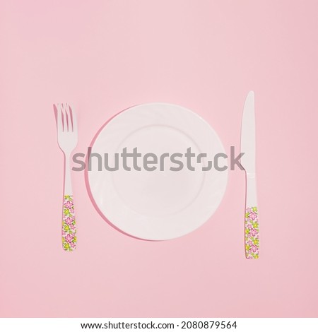 Minimal layout made of plate, fork, and knife on pastel pink background. Holiday party dinner idea.