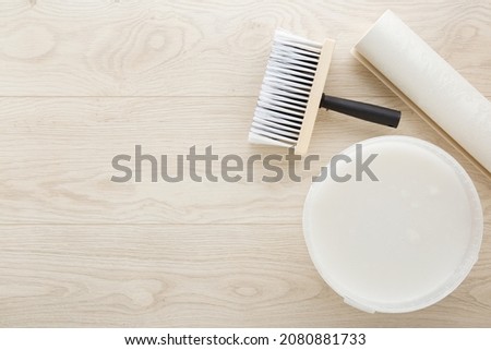 Roll of wallpaper, brush, bucket with glue on light wooden table background. Closeup. Preparation for repair work of home. Empty place for text. Royalty-Free Stock Photo #2080881733