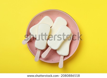 Plate with glazed ice cream bars on yellow background, top view