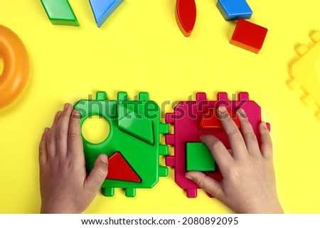 child plays a developmental constructor on a yellow background, hands close-up