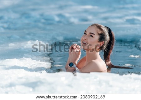 Girl with bikini and a watch in frozen lake ice hole. Woman hardening the body in cold water. Good immunity is protection against many diseases. Vintage color filter Royalty-Free Stock Photo #2080902169