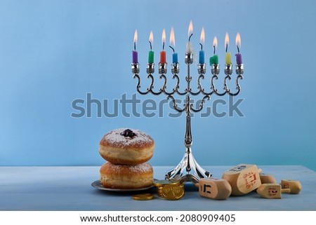 Jewish holiday Hanukkah background with Menorah- traditional candelabra, spinning top Dreidel and Doughnut on blue background