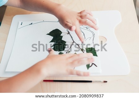 Close up of child sitting at desk and making picture from dry birch leaves. Autumn activities for children