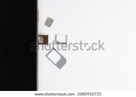 SIM card and mobile phone on white table, top view