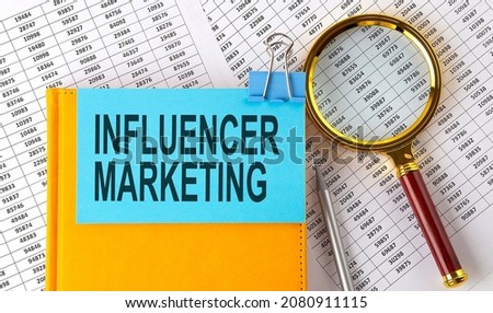 INFLUENCER MARKETING text on sticker on notebook with magnifier and chart. Business