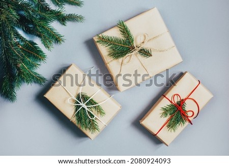 top view of three Christmas gifts in a box decorated with ribbons and a branch of a Christmas tree on a grey background