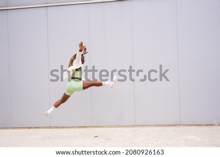 Photo with copy space of an african woman jumping in front of an urban wall