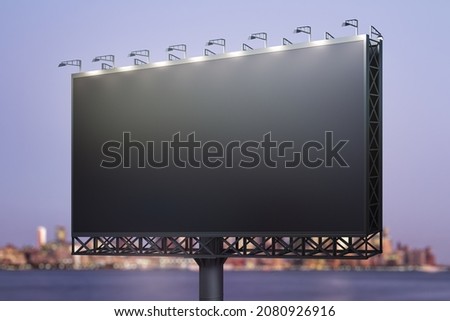 Blank black billboard on cityscape background at evening, perspective view. Mock up, advertising concept