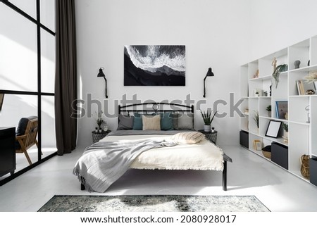 Full view of contemporary bedroom interior design in white tones. Abstract picture hanging on wall. Modern shelves with decor and books. Luxury flat for sale