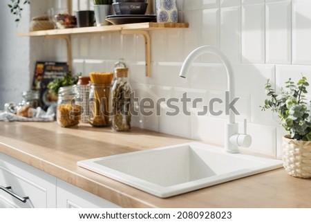 White sink into Scandinavian kitchen interior design in white tones. Wooden shelves with decoration utensils concept. Food products on background Royalty-Free Stock Photo #2080928023