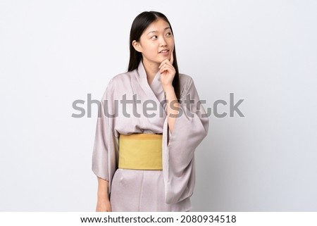Young Chinese girl wearing kimono over isolated background thinking an idea while looking up