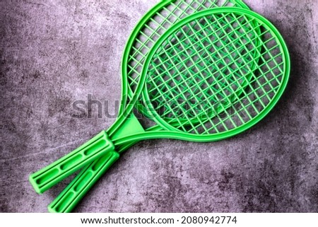 two plastic mesh tennis rackets of juicy green color lie on a worn gray background; as wallpaper for the children's badminton section