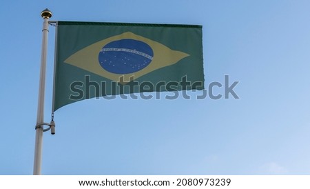 National flag of Brazil on a flagpole in front of blue sky with sun rays and lens flare. Diplomacy concept. International relations. Space for text.
