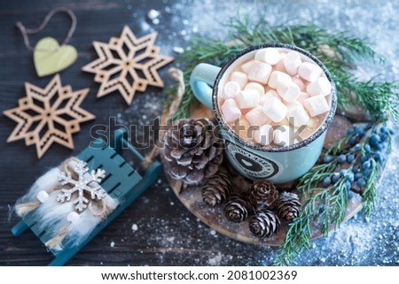 Mug of cacao with small marshmallow, cones on the wooden round tray, decorative wooden sled and snowflakes on the grey wooden background and powder around like snow. Flat lay.