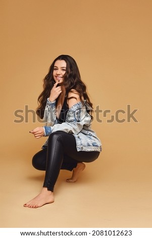 Happy attractive young woman in leggings and denim jacket over beige background
